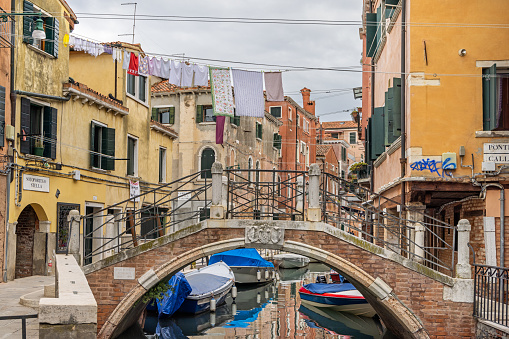Venice, Italy - October 6th 2022: Laundry put out to dry over a old bridge over a narrow canal with moored motorboats in the center of Venice