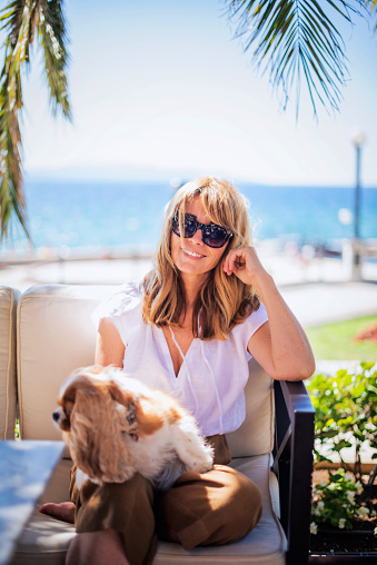 Shot of middle aged woman enjoying sunny day while relaxing by the seaside with her king charles cavalier puppy.