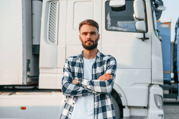 With arms crossed. Young truck driver is with his vehicle at daytime stock photo