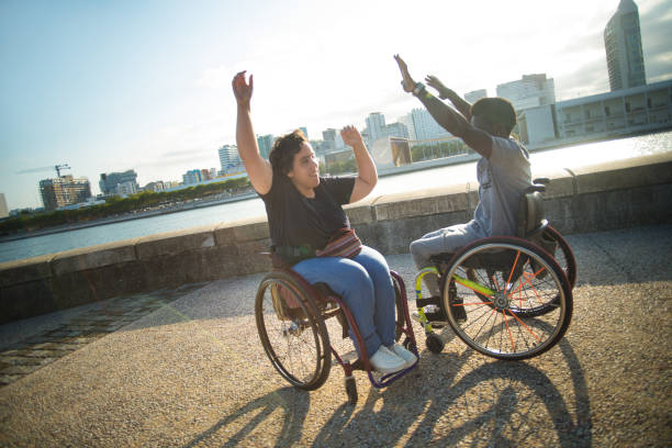 Jolly biracial couple having walk on summer day. African American man and Caucasian woman in wheelchairs on embankment, fooling around. Love, relationship, happiness concept