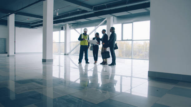 istock Business team talking and looking around modern glass wall building standing inside discussing construction 1436162796