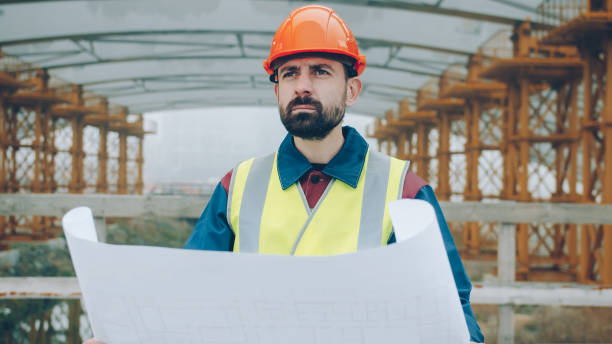 istock Portrait of foreman wearing uniform checking blueprint and looking at construction site outdoors 1436167582