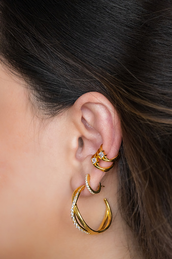 Woman ear with mulriple piercings wearing beautiful earrings with zirconia- details capture.  Beautiful valentine's gift.