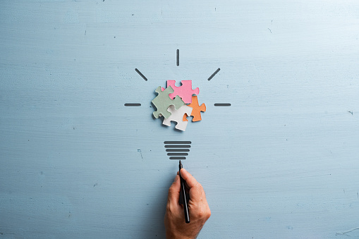 Light bulb made of colorful puzzle pieces and stem and rays cut into blue wooden background in a conceptual image of power and innovation.
