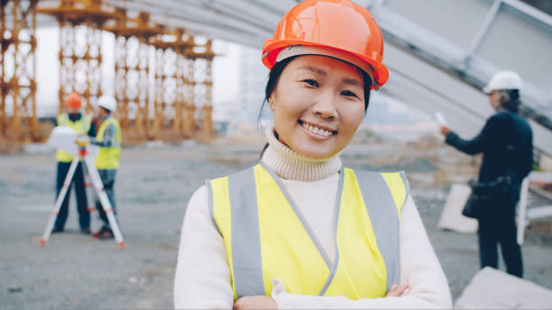 istock Cheerful Asian construction worker wearing uniform smiling at construction site while people working in background 1436170382
