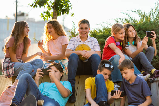 Group of happy children using mobile phones while sitting on the bench stock photo