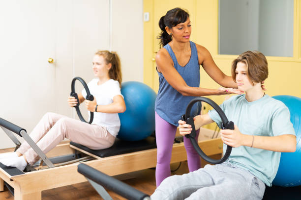 les adolescents effectuent des exercices avec un anneau de gymnastique sous la direction de l’entraîneur - pilates machine photos et images de collection