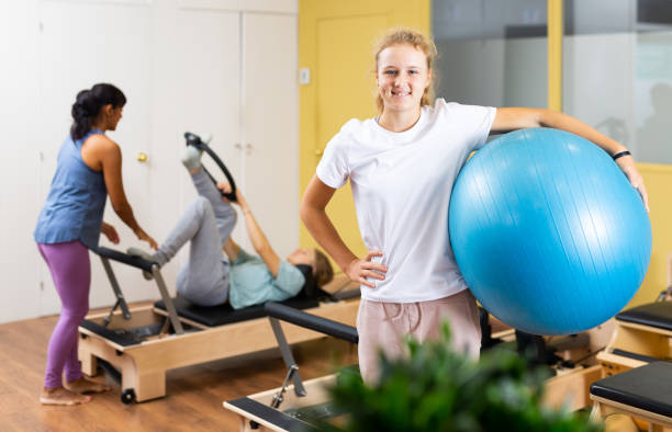 portrait d’une fille debout avec un ballon de fitness pendant un entraînement de pilates au gymnase - pilates machine photos et images de collection