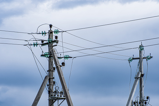 Power poles of high voltage line on cloudy sky background. Electricity transmission.
