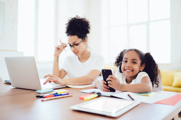 istock Blurred mother using laptop and daughter playing on smartphone while looking at camera 1436176213