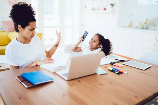 istock Mother stopping daughter from taking picture while working 1436176228