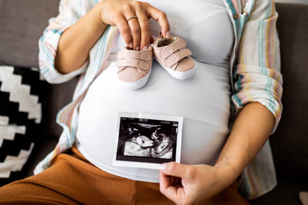 Young pregnant woman looking at baby sonogram holding small baby shoes Pregnant woman resting on sofa first ultrasound stock pictures, royalty-free photos & images