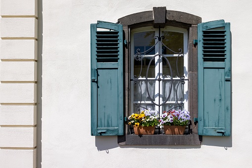 A beautiful blue window with flowerpots and wrought iron fence on a white monastery wall in Germany