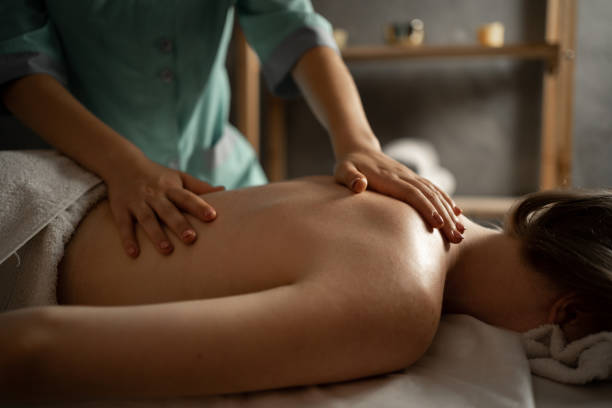 massususe professionnelle faisant un massage thérapeutique. femme profitant d’un massage dans le salon du spa. jeune femme recevant un massage corporel relaxant. soins du corps - massage table photos et images de collection