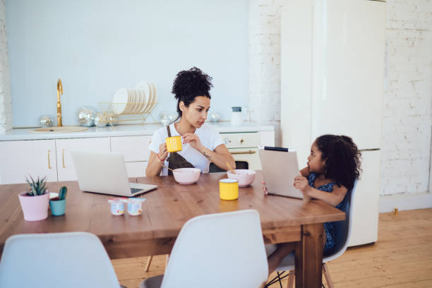 istock Cute little girl having breakfast with young mother while using tablet at home 1436182505