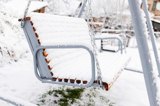 Snow covered wooden white swing after heavy snow. Winter frosty day.