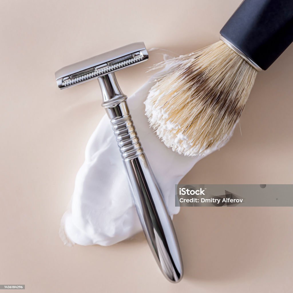 a shaving brush with smeared shaving foam and a t-shaped shaving machine on a beige background. a shaving brush with smeared shaving foam and a t-shaped shaving machine on a beige background. copy space and flatlay. Blade Stock Photo