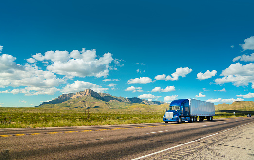 Blue and white semi-truck driving on a rural highway in Texas with El Capitan mountain in the back