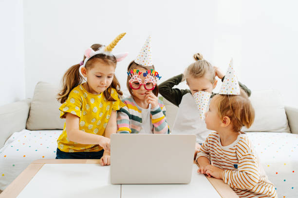 focused tired little kids in party hats gathered around a laptop - birthday child celebration party imagens e fotografias de stock