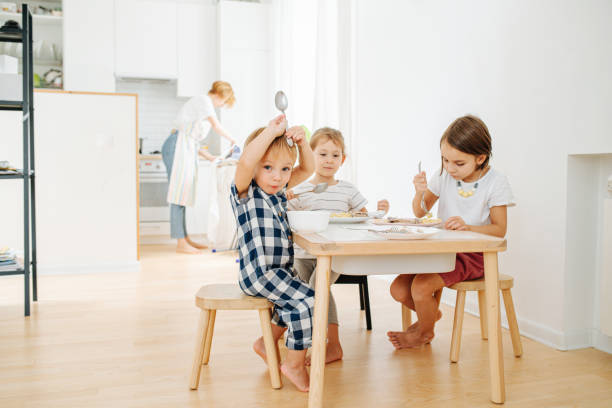 istock Playful little toddler boy sitting behind a kitchen table with his siblings 1436196244