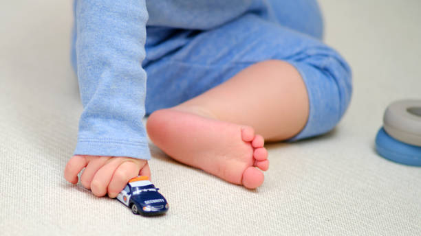 유아 아기는 홈 룸 바닥에서 장난감 자동차를 가지고 놀고 있습니다. 한 아이가 보육원에서 장난감을 가지고 노는 것입니다. 1세 3개월 된 아이 - hands and feet flash 뉴스 사진 이미지