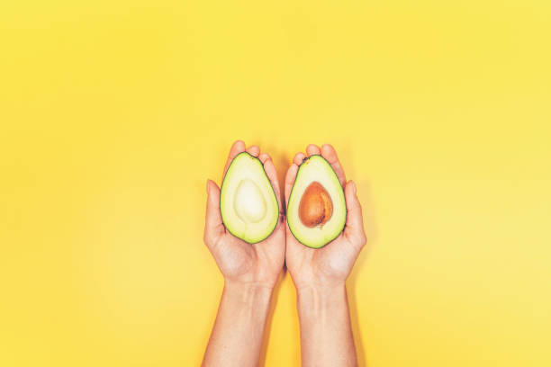 Top view of woman hands holding avocado on yellow background. stock photo