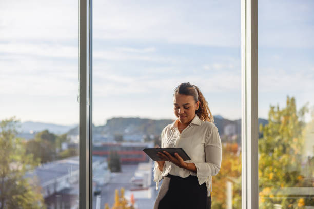istock Portrait Of A Young Hispanic Female Business Professional Using A Digital Tablet While Standing Next To A Window 1436204819