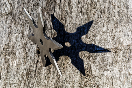 Shuriken (throwing star), traditional japanese ninja cold weapon stuck in wooden background,Silver shuriken with star shape.Samurai, throwing weapons