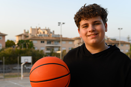 Close-up of a teenager holding a basketball in the park. Lifestyle of a teenager holding a basketball in a park