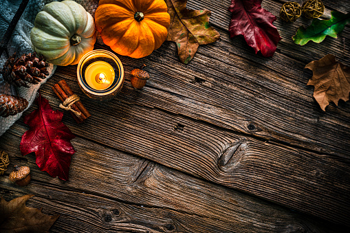 Autumn or Thanksgiving decoration: overhead view of gourds, dry leaves, burning candle, cinnamon sticks, pine cones shot on rustic wooden table. The composition is at the top left of an horizontal frame leaving useful copy space for text and/or logo. High resolution 42Mp studio digital capture taken with SONY A7rII and Zeiss Batis 40mm F2.0 CF lens