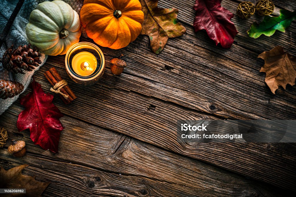 Autumn or Thanksgiving decoration. Copy space Autumn or Thanksgiving decoration: overhead view of gourds, dry leaves, burning candle, cinnamon sticks, pine cones shot on rustic wooden table. The composition is at the top left of an horizontal frame leaving useful copy space for text and/or logo. High resolution 42Mp studio digital capture taken with SONY A7rII and Zeiss Batis 40mm F2.0 CF lens Above Stock Photo