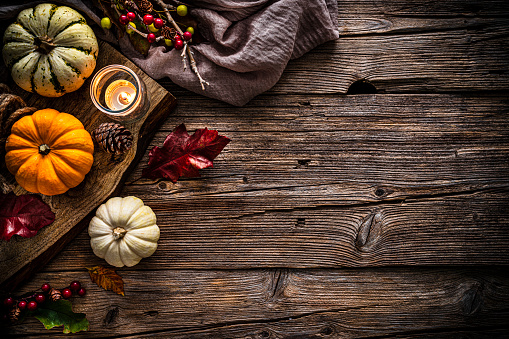 Autumn or Thanksgiving decoration: overhead view of gourds, dry leaves, burning candle, pine cones shot on rustic wooden table. The composition is at the left of an horizontal frame leaving useful copy space for text and/or logo at the right. High resolution 42Mp studio digital capture taken with SONY A7rII and Zeiss Batis 40mm F2.0 CF lens