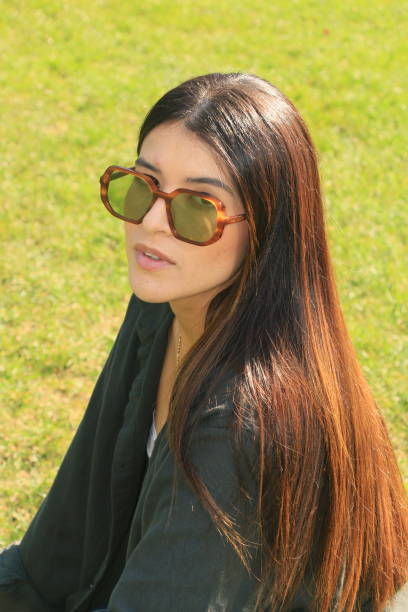 A Colombian woman with sunglasses and a green jacket showing a beautiful head of hair. She has a necklace and sunglasses.
