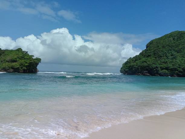 istock Idyllic sandy beach with clouds and forested cliffs in the background in Indonesia 1436207971