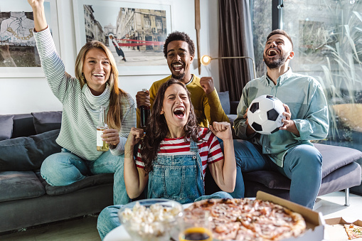 Multiracial group of friends cheering for their sports team and having fun at home