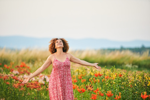 Outdoor portrait of beautiful middle age woman enjoying nice day in lily garden, wearing red dress, happy and healthy lifestyle