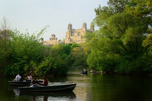 New York, United States – May 01, 2017: A sunny day in New York City with people boating on a pond in Central Park surrounded by lush trees