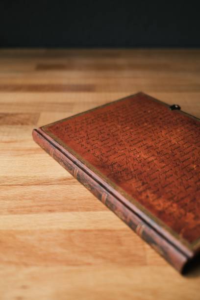 istock Vertical selective focus shot of a vintage leather notebook with an antique design on a wooden table 1436214610