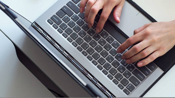 istock close-up, women's hands are typing something on a gray laptop keyboard, on a white desktop. 1436216034