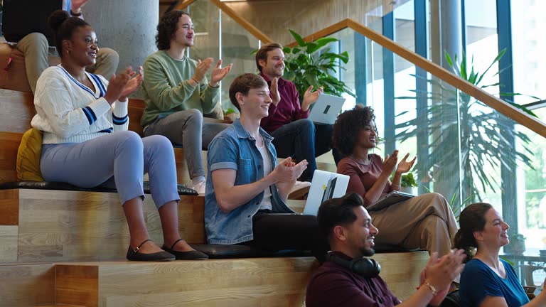 Multi-ethnic group of people sitting on steps applauding during a conference