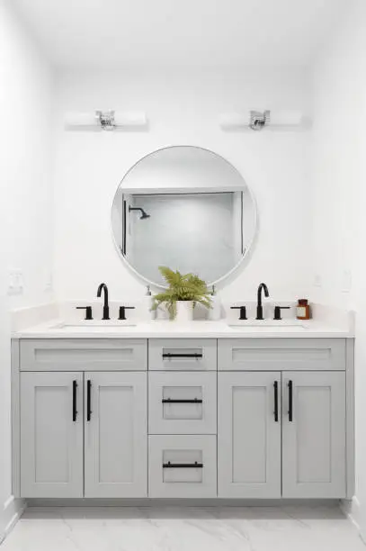 Photo of A bathroom with a grey vanity and circular mirror.