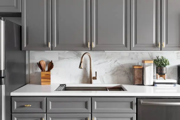 Photo of A grey kitchen with a gold faucet and marble subway tile.