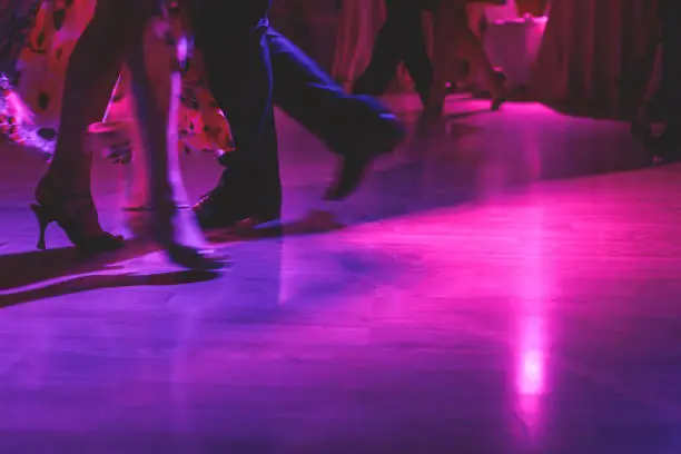 Dancing shoes of a couple, couples dancing traditional latin argentinian dance milonga in the ballroom, tango salsa bachata kizomba lesson, festival on wooden floor, purple, red and violet lights