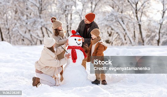 istock Happy children sculpting funny snowman together with parents in winter snow-covered park 1436228281