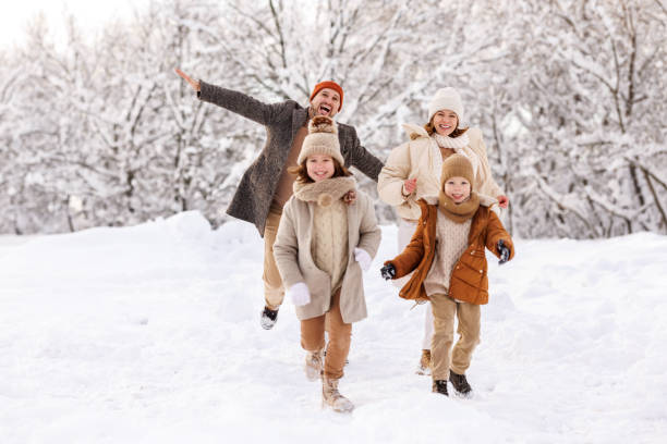 szczęśliwe dzieci bawią się z rodzicami na świeżym powietrzu w zimowym parku, rodzina cieszy się śnieżną pogodą w lesie - family winter walking fun zdjęcia i obrazy z banku zdjęć