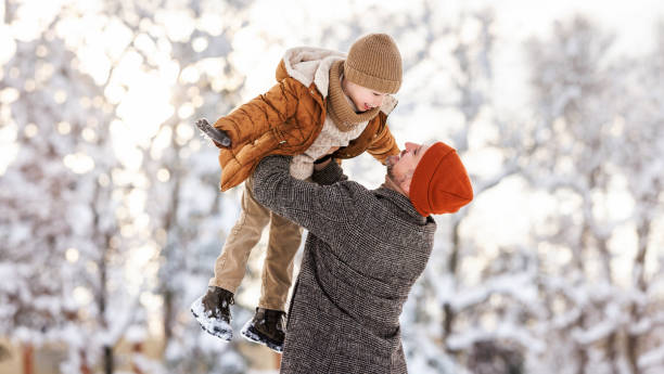 Father lifting little son up while having fun together outdoor on frosty day, happy dad and kid playing in winter park, enjoying snowy weather, actively spending New year holidays on fresh air