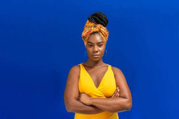 молодая женщина в красочной длинной одежде на синем фоне. - serious african ethnicity mid adult portrait стоковые фото и изображения