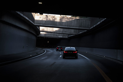 Black car is driving down the road in the tunnel. Modern highway tunnel underpass. Traffic infrastructure, tunnel architecture, light effect.