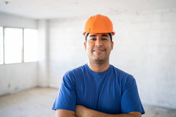 A construction worker in a yellow hard hat is carefully measuring with a tape measure, showcasing his work attire