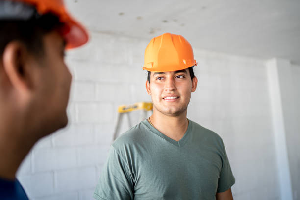 A construction worker in a yellow hard hat is carefully measuring with a tape measure, showcasing his work attire